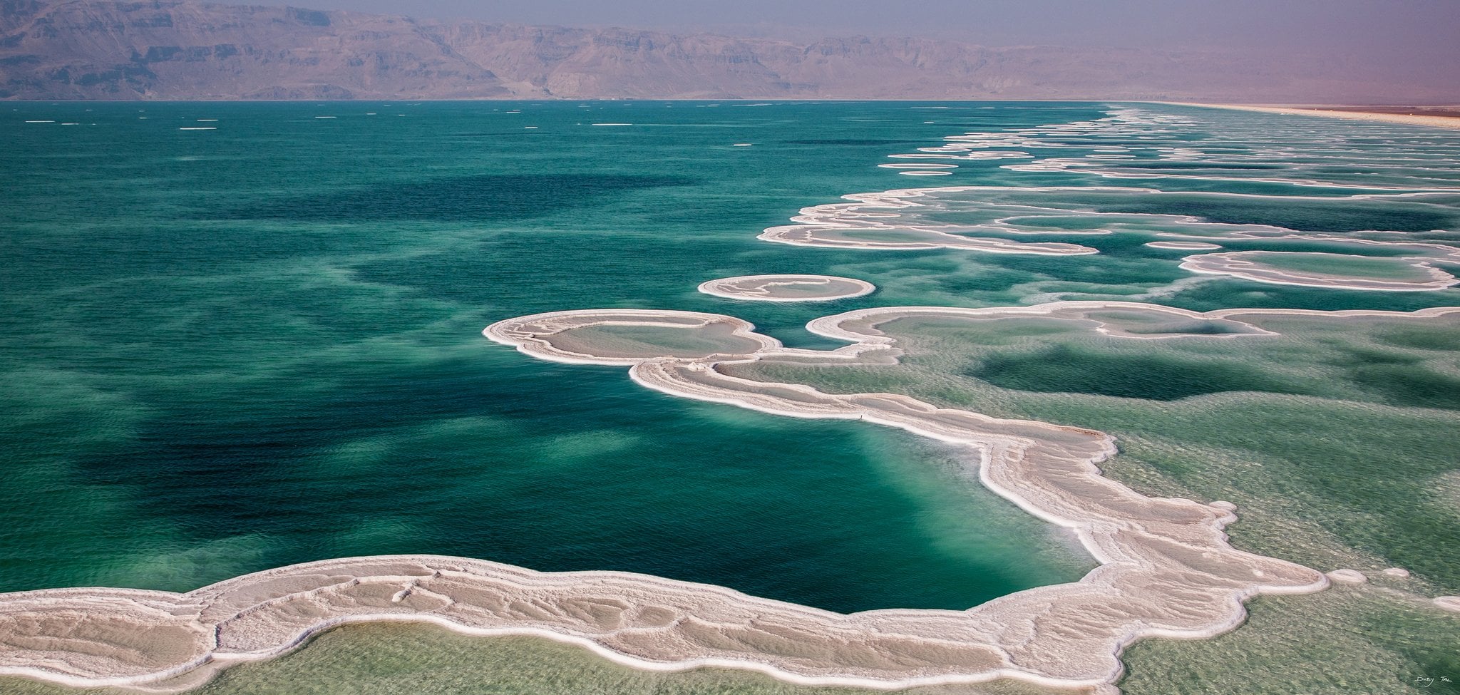 Turquoise Dead Sea water beside white salt deposits and desert hills
